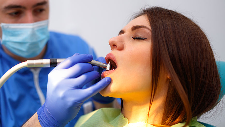 A woman with her mouth open as a dentist drills one of her teeth.